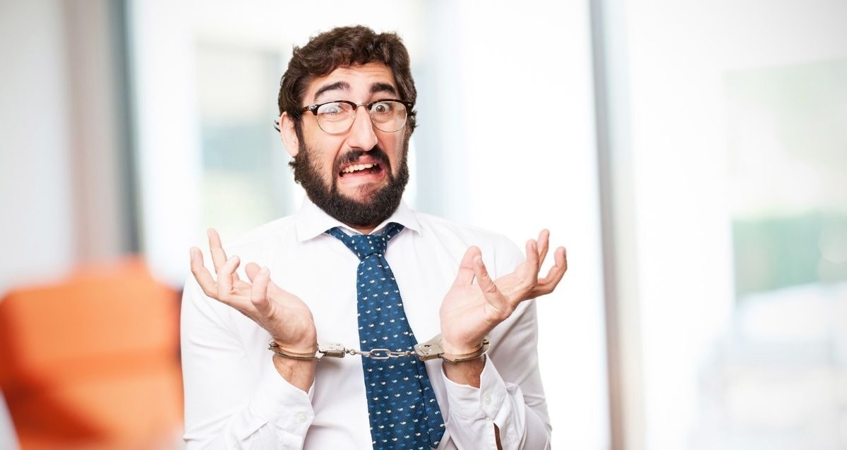 manager in camicia e cravatta con le manette e l'espressione sorpresa